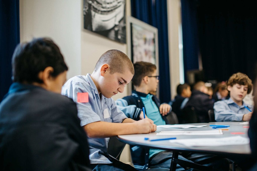 A table of boys in school uniforms are focused and writing on paper.