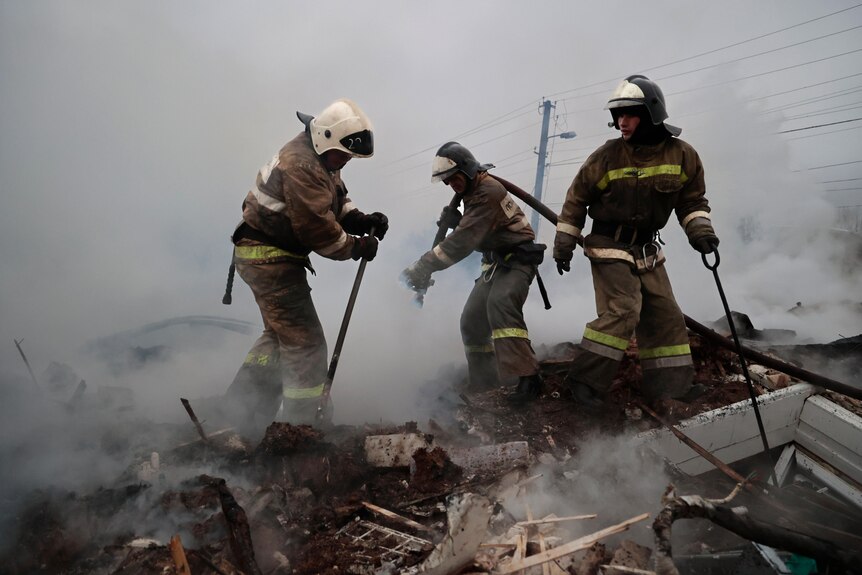 Three firefighters search through smoking debris after Russian shelling.
