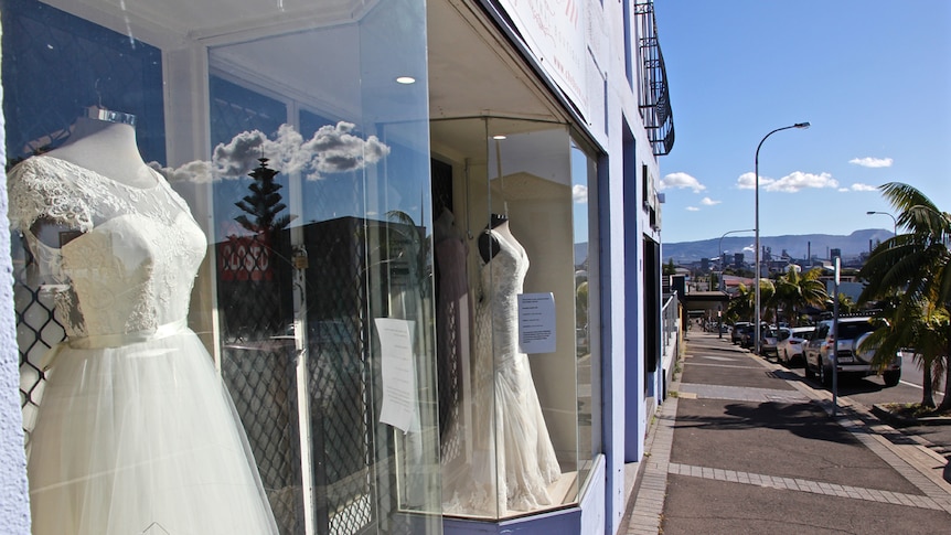 Dresses in the window of a Port Kembla bridal store with clouds in the window's reflection.