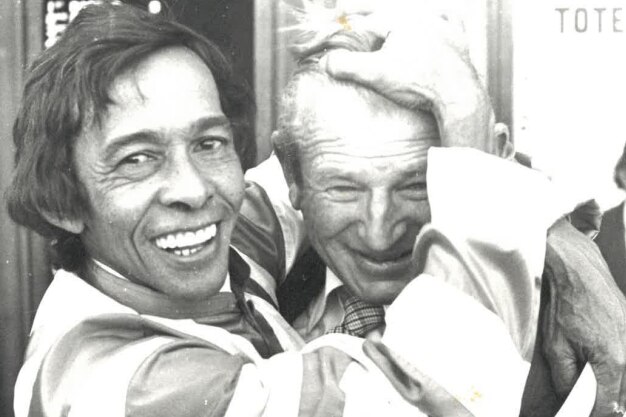 A black and white photo of a jockey hugging a man in a suit
