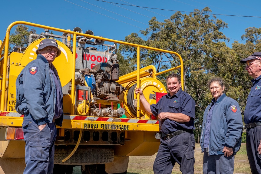 Four people stand behind a fire truck.