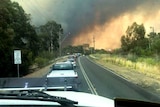 A view from the inside a vehicle looking to a traffic jam in front and bushfire smoke in the distance.