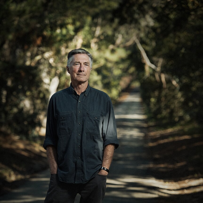 Garry Disher standing on a tree-lined path, facing the camera. Garry is wearing a dark shirt with the sleeves rolled up.