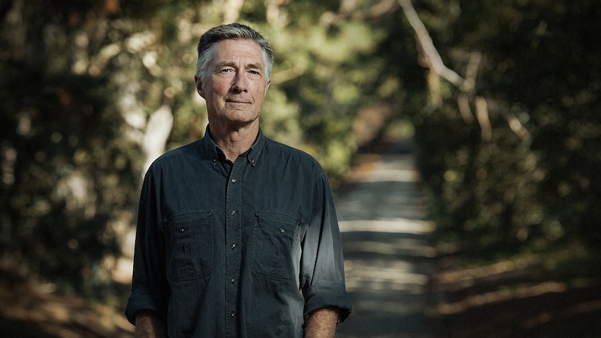 Garry Disher standing on a tree-lined path, facing the camera. Garry is wearing a dark shirt with the sleeves rolled up.
