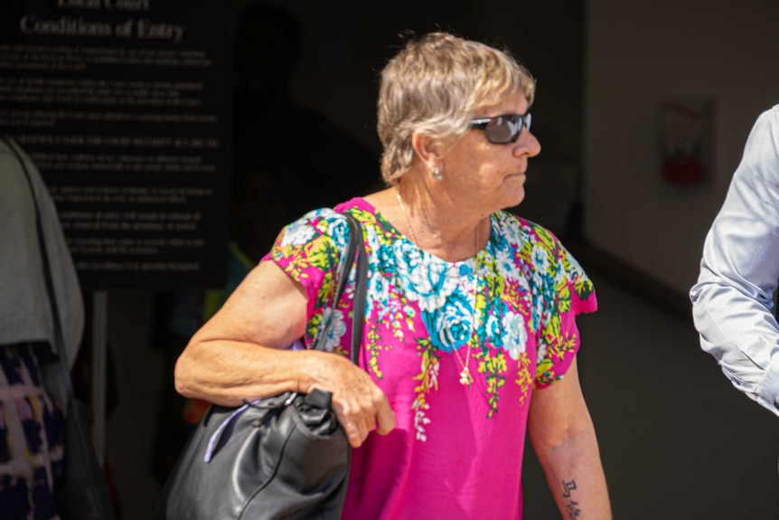 Bronwyn Buttery is wearing a pink dress and leaving Darwin Local Court. She is wearing glasses and looks serious.