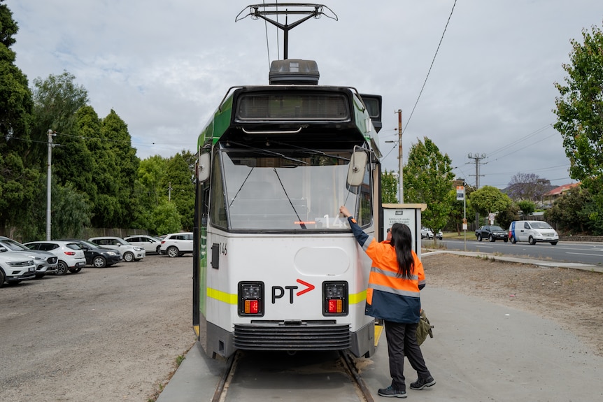 Patricia Santiago, a young woman of Filipino appearance, wears high-visibility clothes and drives a tram