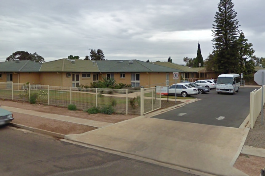 A blonde brick building with a carpark and driveway.