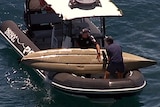 Police officers in a boat pull a kayak from the water off Moffat Beach. What appear to be puncture wounds can be seen.