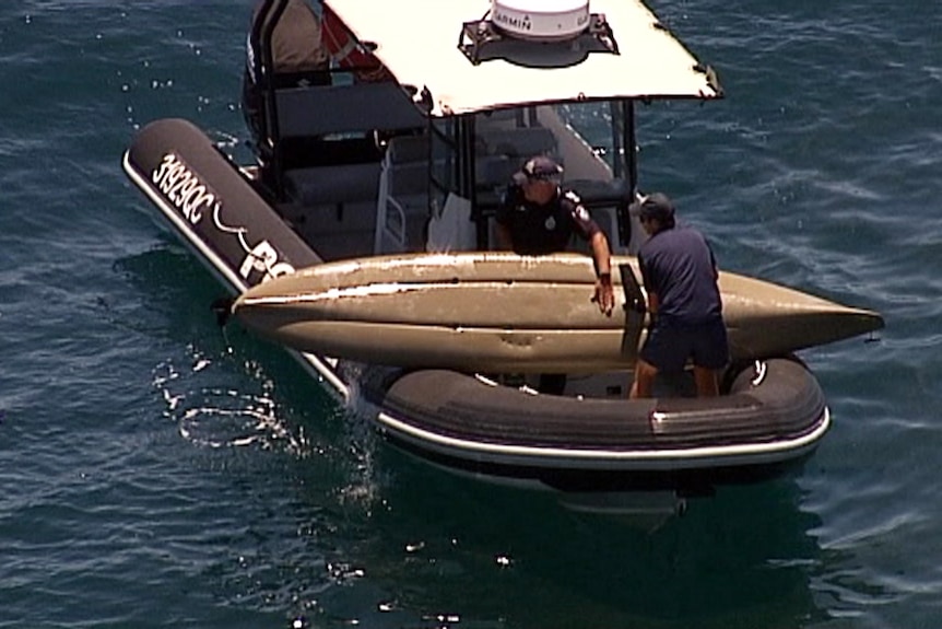 Police officers in a boat pull a kayak from the water off Moffat Beach. What appear to be puncture wounds can be seen.