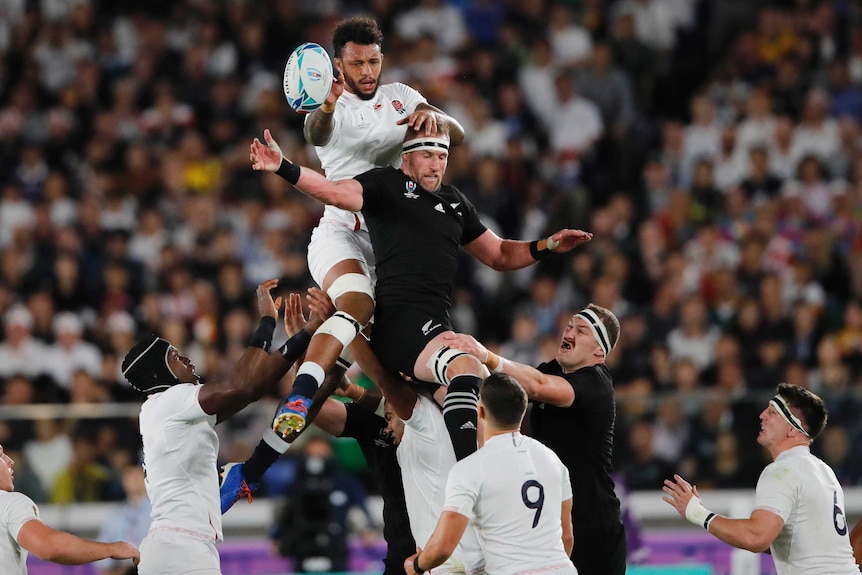 An England rugby union player wins line-out ball against an All Blacks opponent in their Rugby World Cup semi-final.