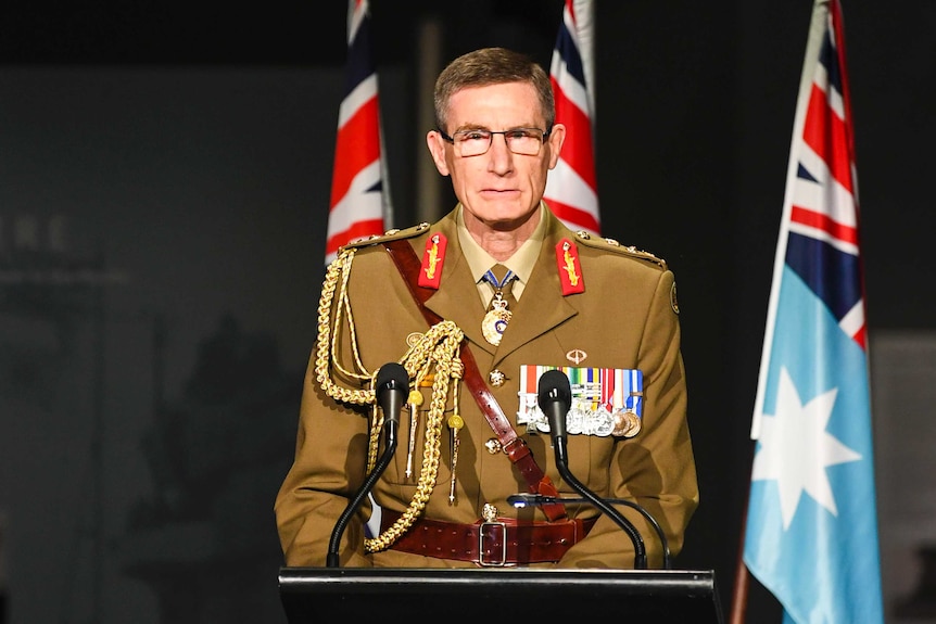 A man in military uniform with medals stands at a podium.