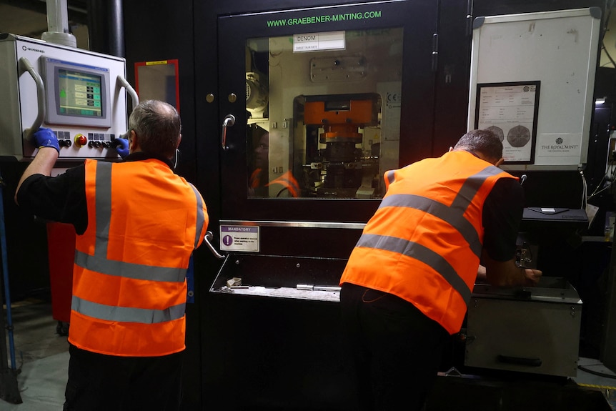 Two men in high vis vests in front of a coin machine