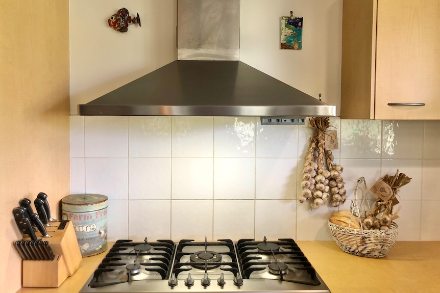 Three garlic braids hanging beside a stove with more sitting with bread in a basket.