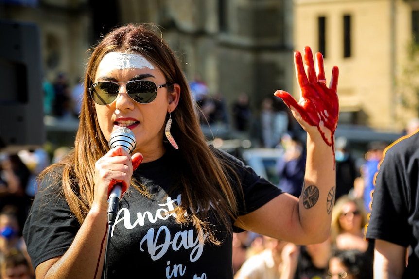 Greens senator for Victoria Lidia Thorpe with fake blood on her hands, holding a microphone.
