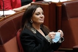 Jacqui Lambie sitting in the senate holding a face mask 