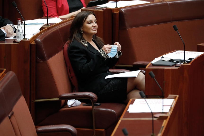 Jacqui Lambie sitting in the senate holding a face mask 