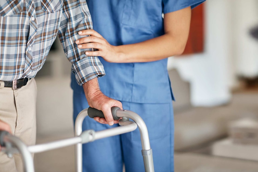 A carer assisting her elderly patient who's using a walker for support