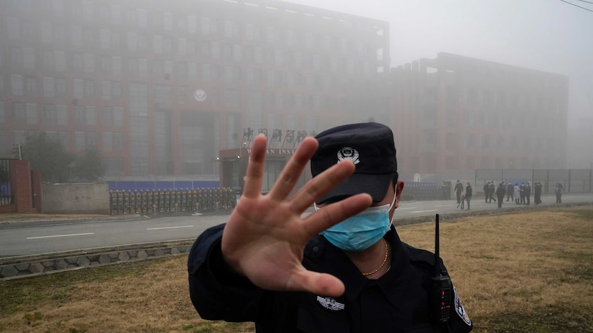 A security person moves journalists away from the Wuhan Institute of Virology