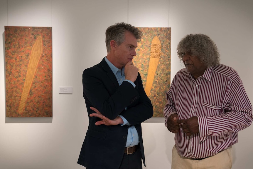 An artist and gallery director chat in front of paintings in the Lismore Regional Gallery