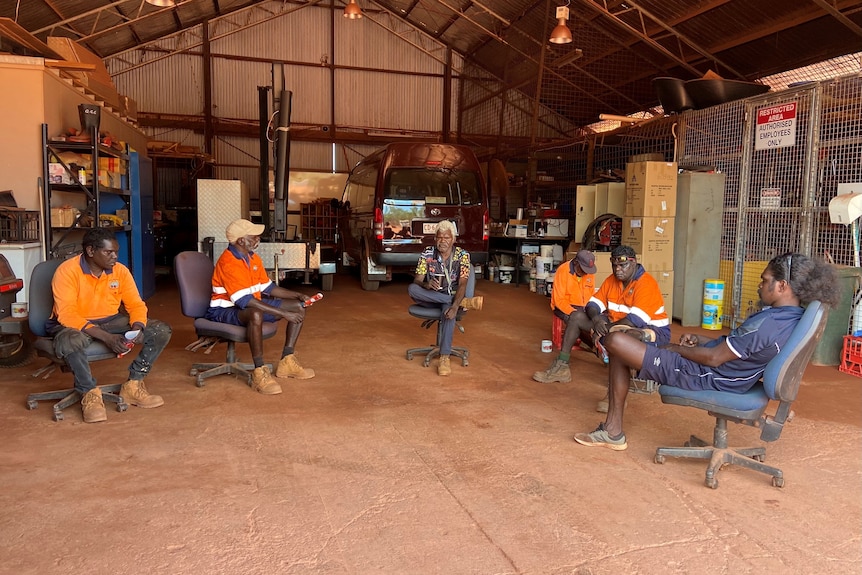 Six men sit on chairs in a shed in a remote community in the Northern Territory. 