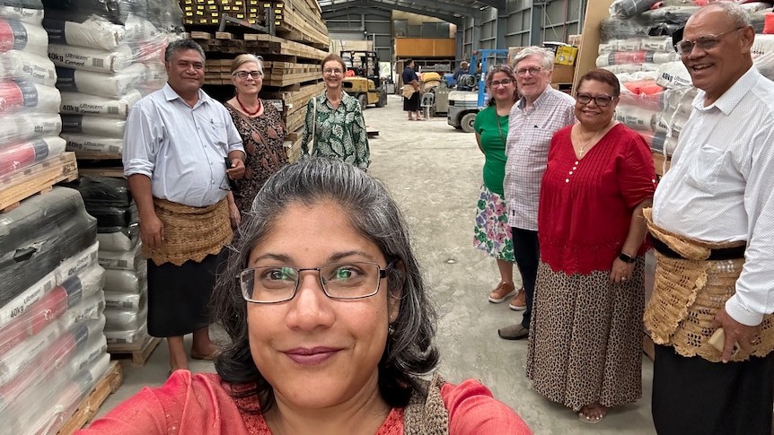 A photo of Dr Goringe inside a shed in Pacific with food donations, other members of the community standing behind her.