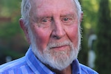 A headshot of an older man with a white beard wearing a blue checked shirt.