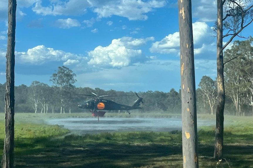 A helicopter collects water from a pond as part of fire fighting efforts.