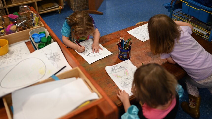three children at daycare sit around a desk and draw