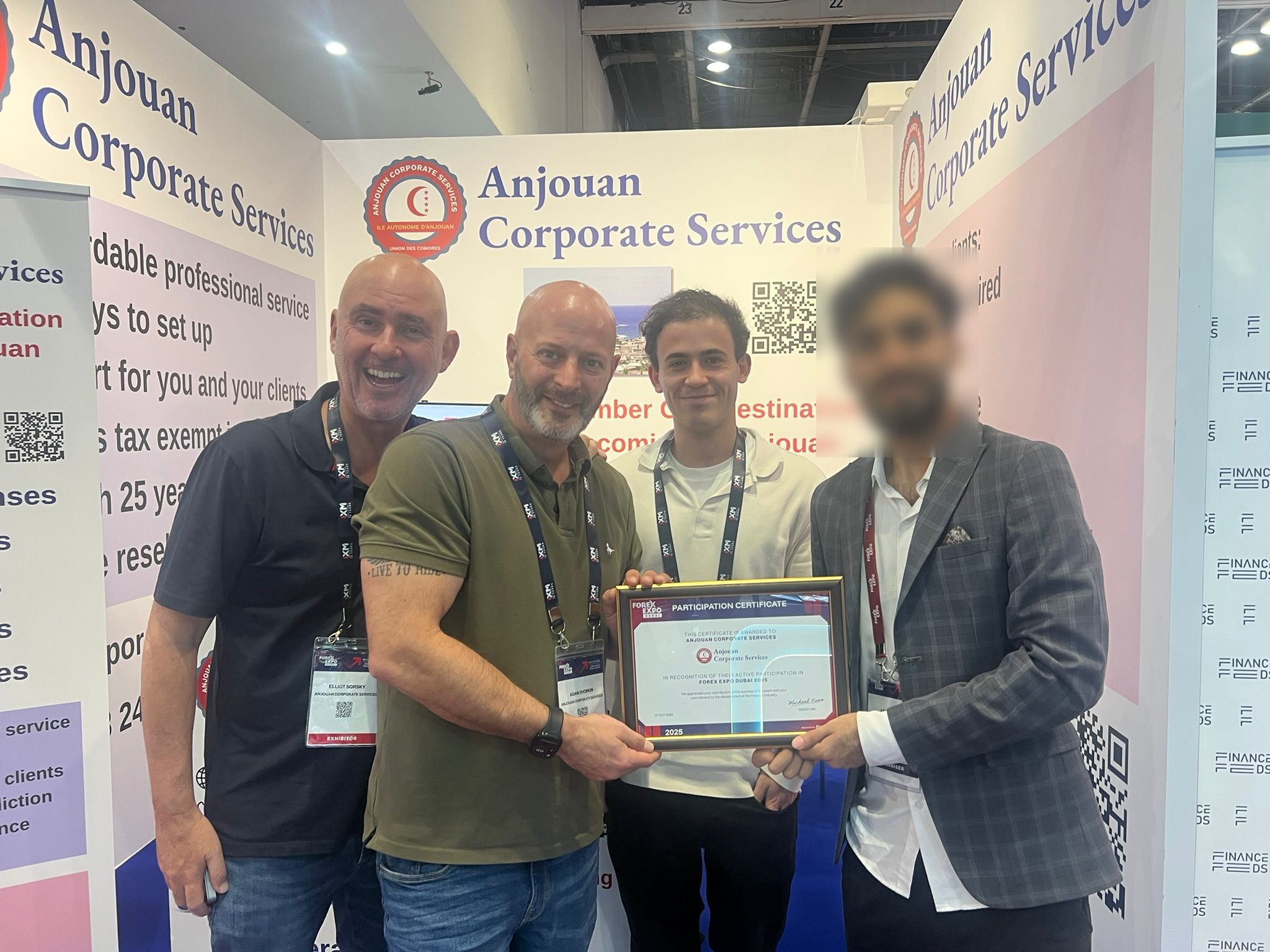 Quatro homens (um deles com o rosto desfocado) estão em uma cabine de conferência sob o logotipo da Anjouan Corporate Services.