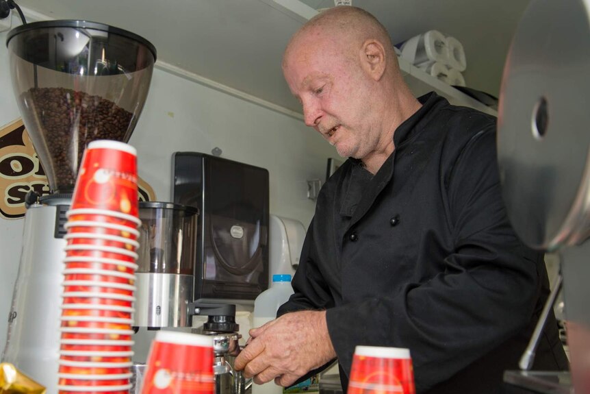 Mission Australia client Walter Humphreys grinds coffee beans and tamps the ground coffee into the basket.