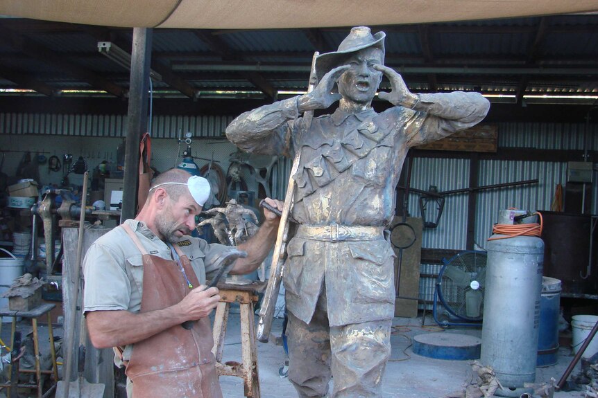 Sculptor Brett Garling chips away at a bronze statue of a soldier.