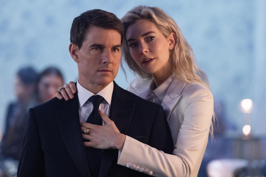 Vanessa Kirby, a blonde white woman in a white jacket, wraps her arms around Tom Cruise, a brunette white man in a suit.