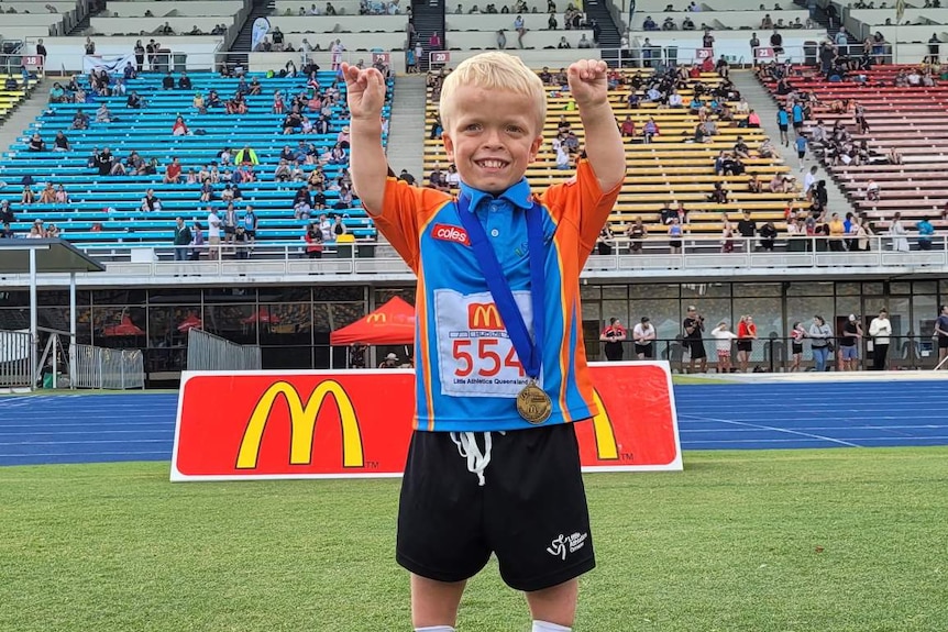 boy holding hands up with medal around neck