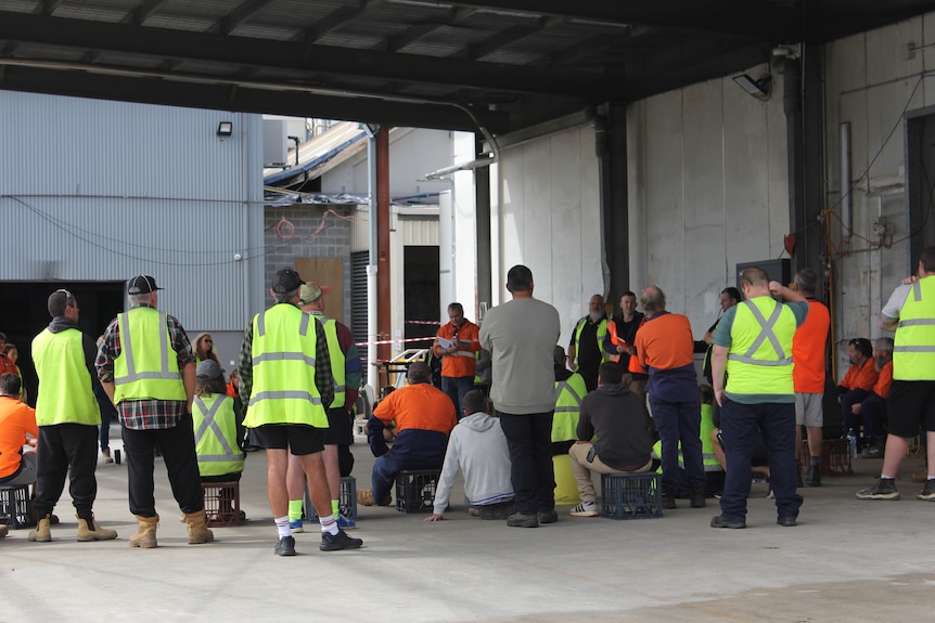 A group of workers in hi-vis gather around union secretaries in a factory.