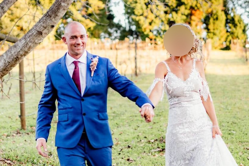A man in a blue suit walks hand in hand with a woman in a wedding dress whose face has been blurred for privacy.