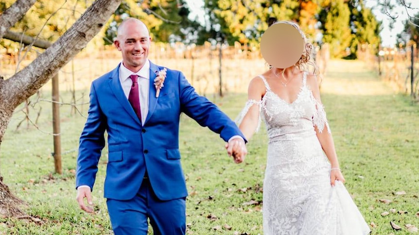 A man in a blue suit walks hand in hand with a woman in a wedding dress whose face has been blurred for privacy.