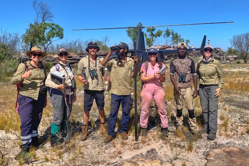 A group of seven people standing next to each other and looking at the camera, with most dressed as rangers, in the bush.