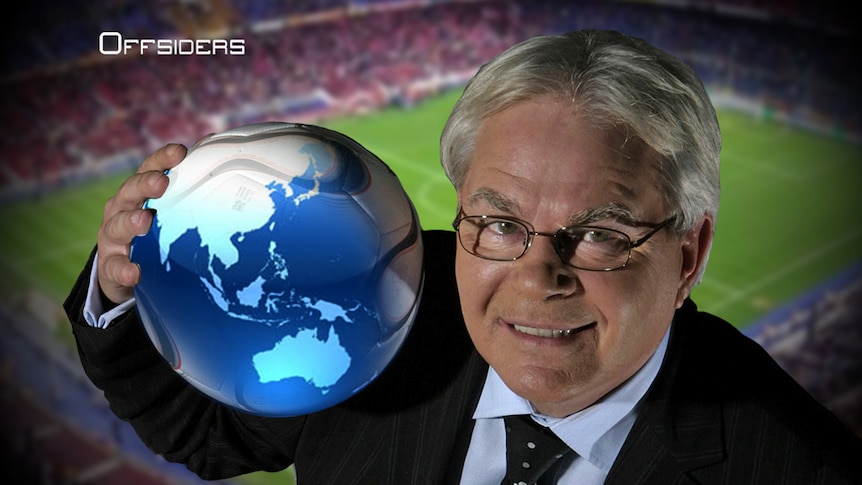 Les Murray holds a soccer ball with a globe superimposed on it.
