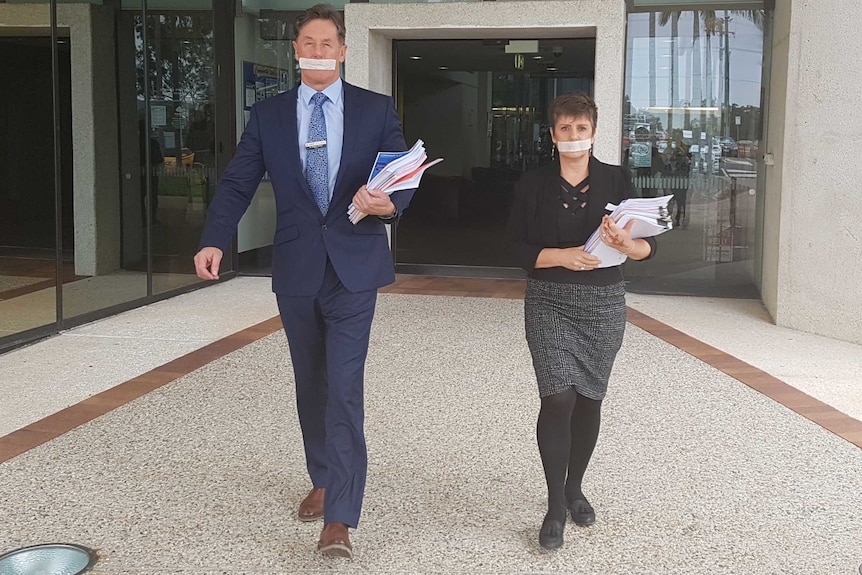 Darren Power and Lisa Bradley with tape over their mouths leaving Logan council chambers