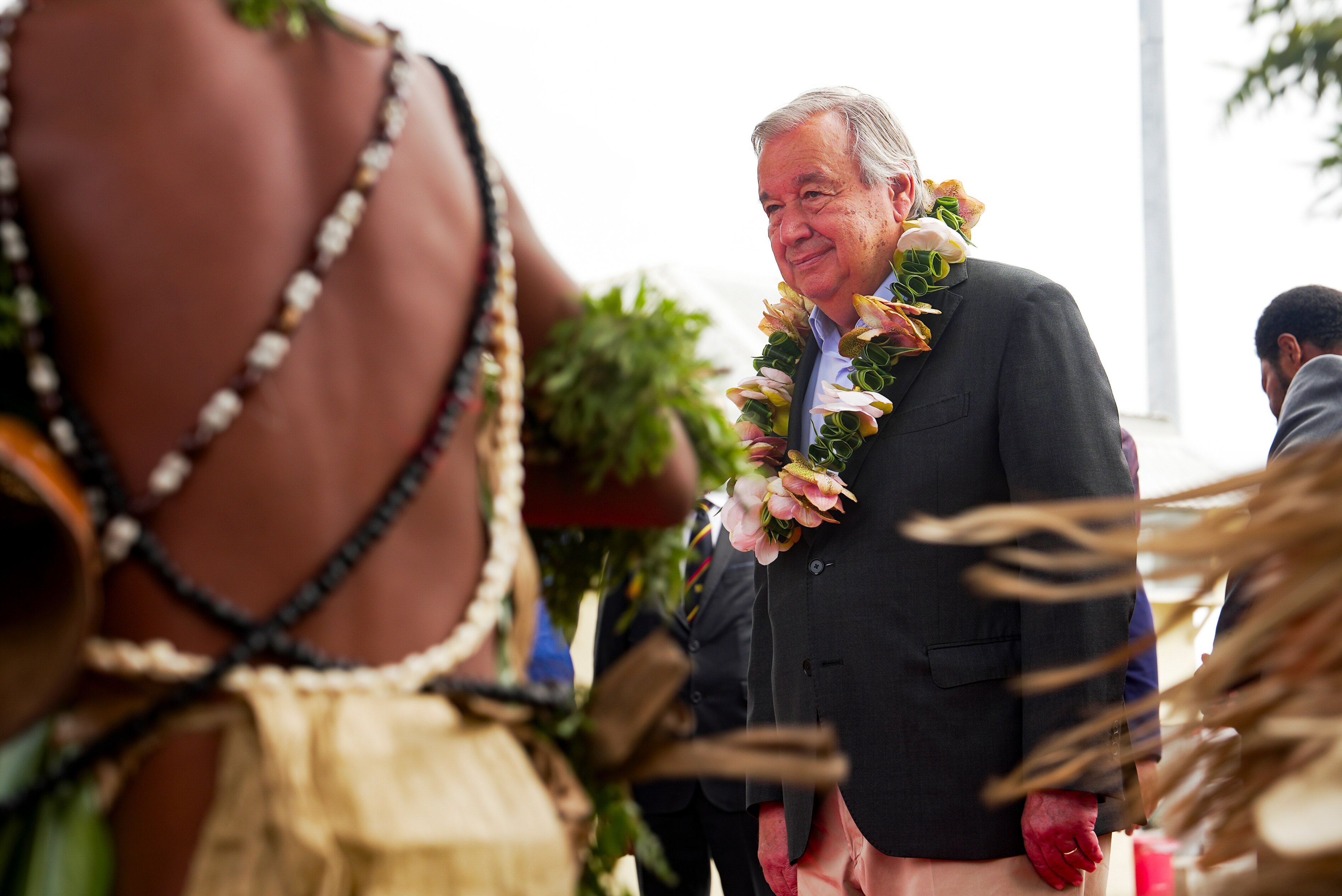 A man in a suit wears a flower necklace while smiling