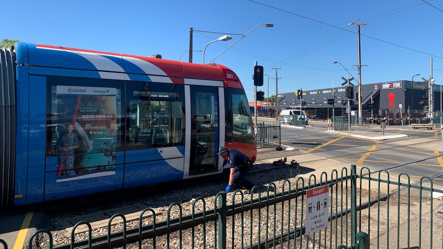 A police officer kneeling down to assess a red and blue tram