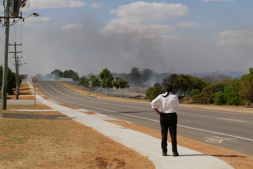 A woman stands looking down Abraham street in Utakarra, Geraldton, as smoke from a bushfire rises.