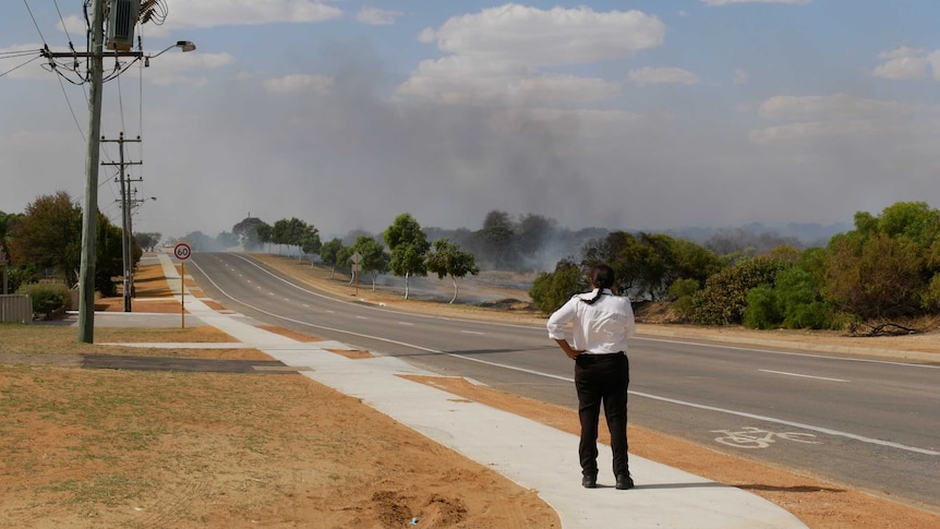 A woman stands looking down Abraham street in Utakarra, Geraldton, as smoke from a bushfire rises.