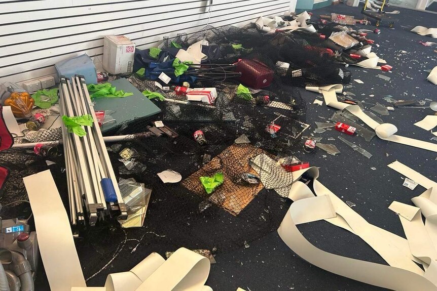 Broken glass, blinds and belongings cover the floor of a room.