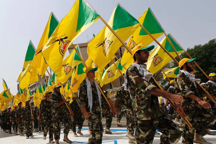 Kataib Hezbollah wave the party's flags as they walk along a street painted in the colours of the Israeli flag.