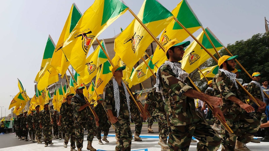 Kataib Hezbollah wave the party's flags as they walk along a street painted in the colours of the Israeli flag.