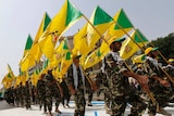 Kataib Hezbollah wave the party's flags as they walk along a street painted in the colours of the Israeli flag.