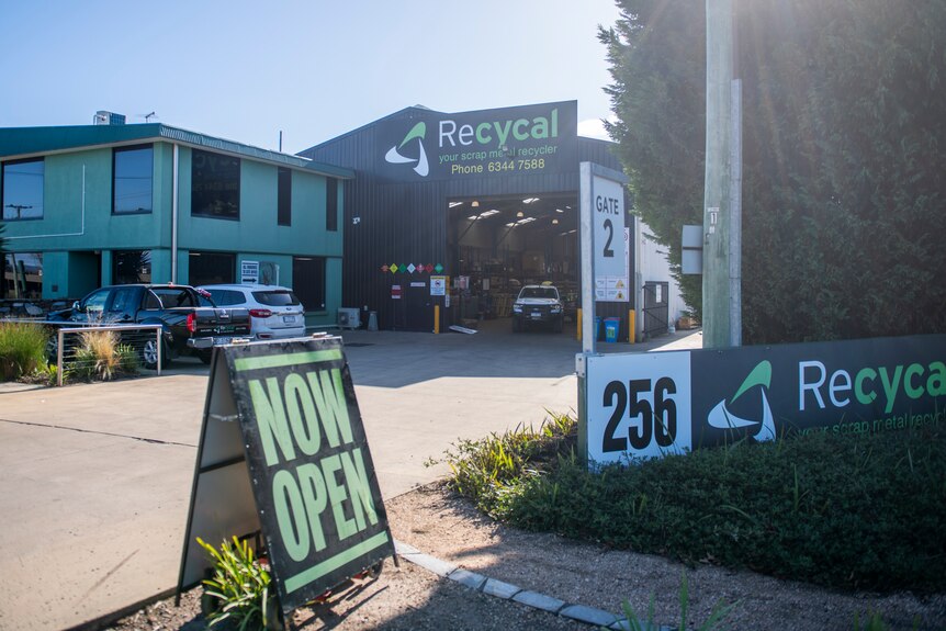 The exterior of Recycal's building with "now open" sign with green lettering.