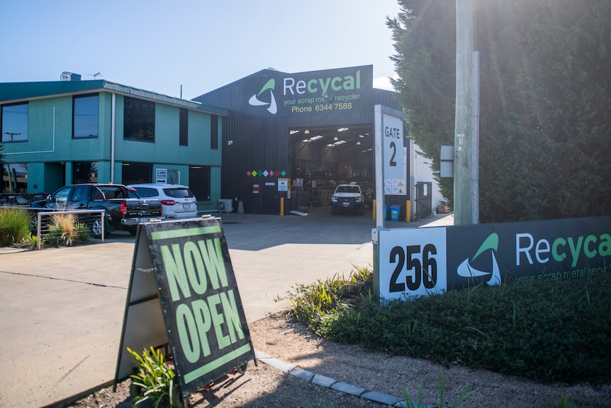 The exterior of Recycal's building with "now open" sign with green lettering.