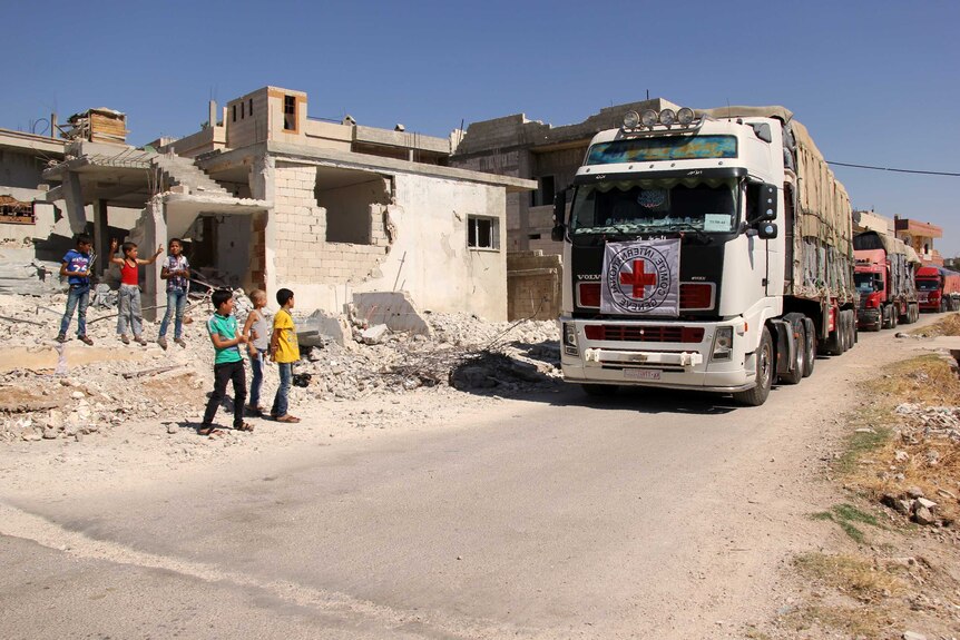 Syrian children stand on the side of a road watching a 48-truck convoy